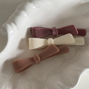 Three acetate bow hair clips in pink white and brown colors on a decorative plate