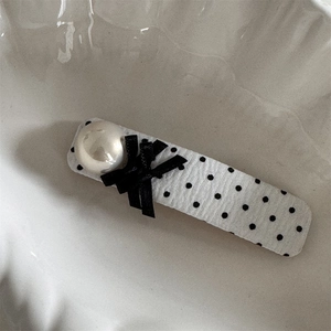 Detailed shot of a vintage polka dot hair clip with faux pearl and satin black bow