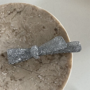 Macro shot of a silver glitter bow hair clip on a marble tray with metallic texture detail