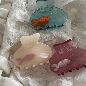 Dettaglio di tre mollette per capelli a forma di pesce nei colori blu, crema e viola