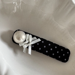 Detailed view of polka dot bow hair clip with faux pearl and black fabric texture