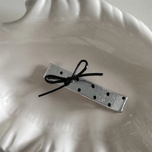 Close-up of silver metal hair clip with black polka dots and a delicate bow detail