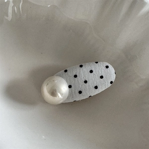 Detailed view of polka dot pattern hair clip with large pearl embellishment on tray