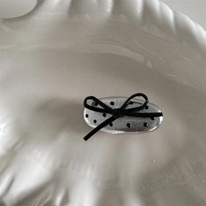 Detail of silver polka dot hair clip with black ribbon bow on white ceramic plate