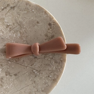 Detail view of a matte pink acetate bow hair clip on a marble tray for hair styling
