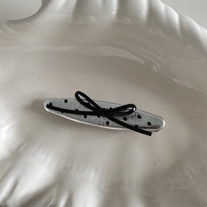 Detail view of silver polka dot bow hair clip on a white shell-shaped ceramic plate