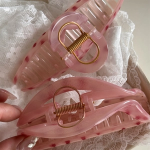 Macro detail of large pink marble resin hair claws with premium gold-tone metal springs