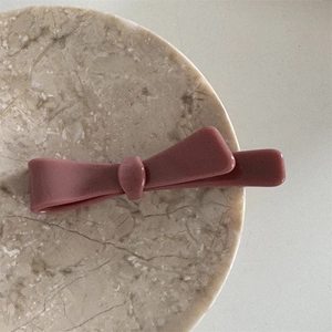 Macro view of dusty rose acetate bow hair clip with matte silk texture on marble tray