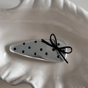 Close-up of silver polka dot hair clip with black bow detail in a white shell tray