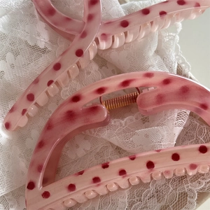 Close-up of pink polka dot hair claw clip with metal spring on white lace background