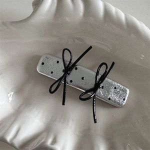 Detail view of silver metal hair clip with black leather bows and polka dots on shell tray