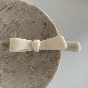 Detail of cream white acetate bow hair clip on a natural marble tray background