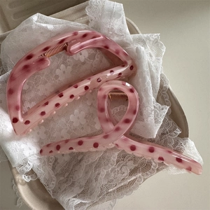 Close-up of pink polka dot hair claw clips on white lace, featuring resin texture