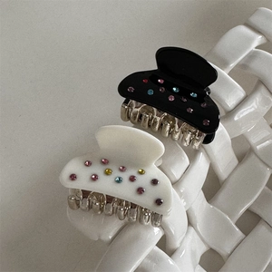 Dettaglio di piccoli fermagli per capelli neri e bianco perla con strass colorati su metallo