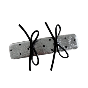 Silver metallic hair clip with black polka dots and bows on a white background