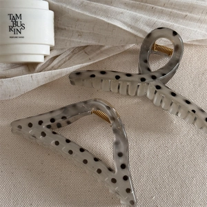 Detail view of gray polka dot hair claw clips with golden springs on soft fabric