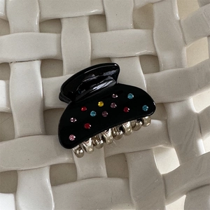 Dettaglio molletta per capelli nera con strass colorati su sfondo bianco strutturato