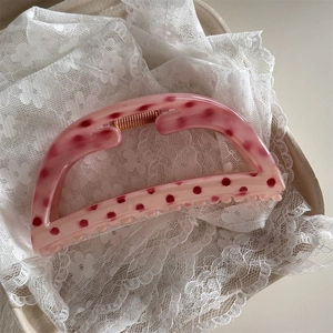 Close-up of pink polka dot hair claw clip with metal spring on white lace