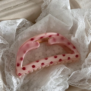 Detailed view of pink polka dot hair claw clip on white lace fabric with gold spring