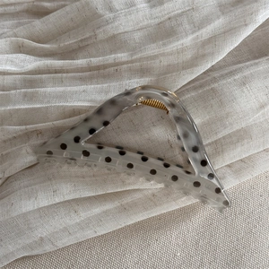 Detail of a translucent cream triangular hair claw with black polka dots on linen fabric