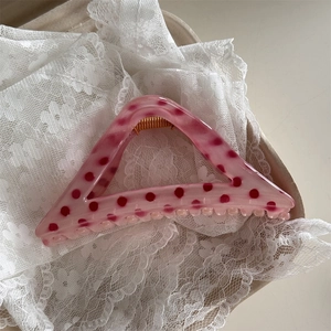 Detail of pink polka dot hair claw clip resting on white lace fabric background