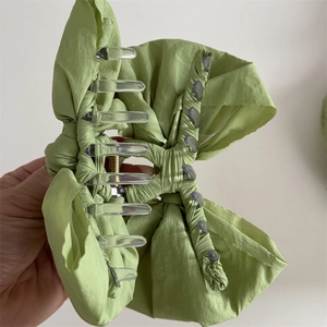 Detail of light green fabric bow hair claw clip featuring transparent teeth and spring