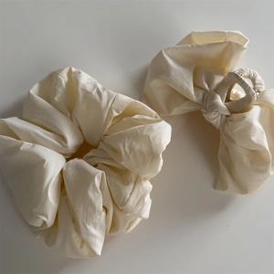 Detail view of cream fabric bow hair claw and matching scrunchie set on grey background