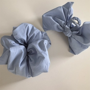 Detail view of light blue fabric hair scrunchie and bow claw clip set with matte texture