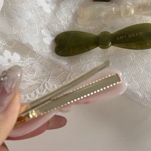 Détail macro d'une barrette à nœud en acétate rose avec logo doré sur de la dentelle