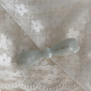 Détail d'une barrette à cheveux nœud en acétate ivoire avec logo doré sur de la dentelle
