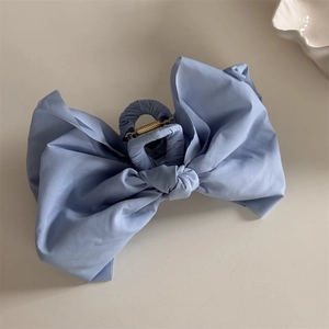 Macro view of light blue fabric bow hair claw clip with sturdy golden metal spring