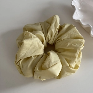 Macro detail of a light yellow pleated fabric scrunchie on a minimalist white background