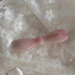 Détail d'une barrette nœud en résine rose marbrée avec logo doré sur fond de dentelle