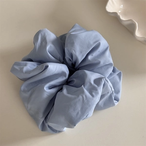 Detail of light blue oversized fabric scrunchie with soft pleated texture on white background