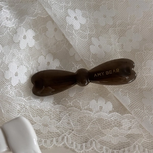 Détail de pince à cheveux nœud marron à texture marbrée avec lettrage doré sur dentelle