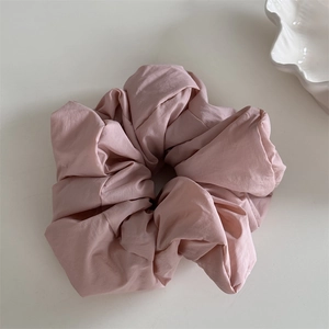 Detail of light pink fabric scrunchie with soft pleated texture on a cream background