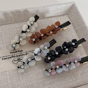 Floral acetate hair clips with rhinestones in five colors on a beige textile tray
