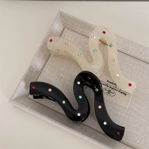 Detail showing two wave-shaped hair clips in cream and black with colorful rhinestones