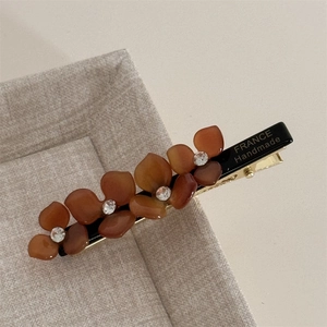 Detailed close-up of brown acetate floral hair clip with crystal rhinestones on a metal grip