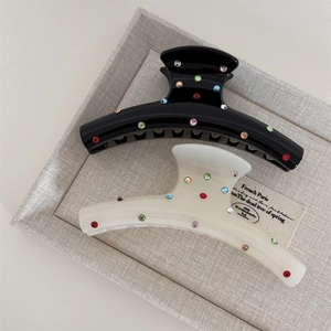 Close-up of elegant hair claw clips with colorful rhinestones on polished black and white surfaces