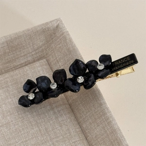 Detail of golden metal hair clip with France Handmade engraving and black acrylic petals