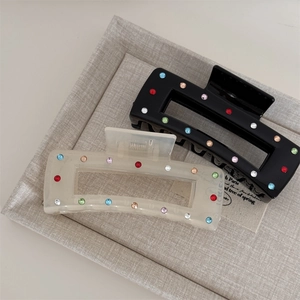 Close-up of black and cream hair claw clips with colorful rhinestones on a display tray