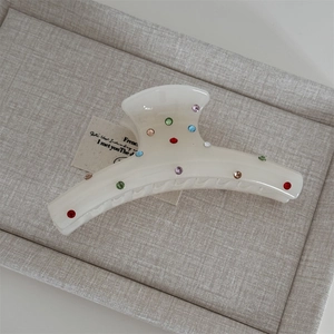 Detailed close-up of cream white hair claw clip with colorful rhinestones on fabric