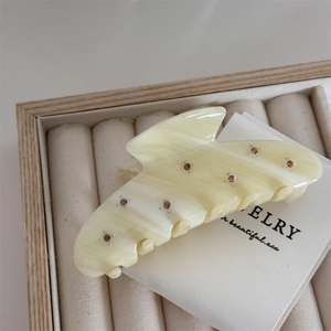 Detail of a large cream acetate hair claw clip with rhinestones and marble texture