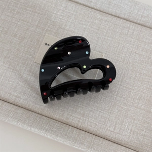 Close-up of black heart-shaped hair claw clip with colorful rhinestones on fabric surface