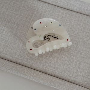 Macro detail of creamy acetate hair claw clip with colorful rhinestones on textile background