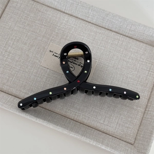 Close-up of black claw clip with colorful rhinestones on a textile background tray