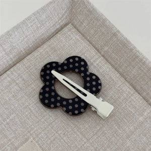 Detailed view of flower-shaped hair clip with black and white polka dots and metal duckbill clip