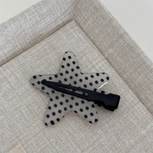 Macro view of a gray star-shaped hair clip with black polka dots and metal duckbill clip
