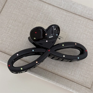 Detail of a black hair claw clip featuring colorful rhinestones and a heart-shaped design